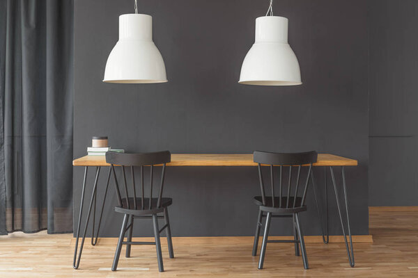 Black chairs at wooden table under white lamp in minimal dining room interior with curtain