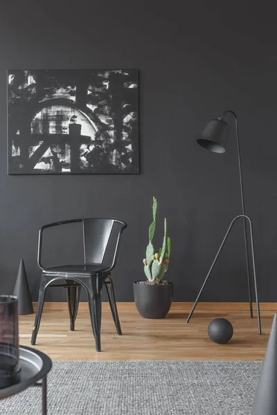 Painting on the black wall, metal chair and green cactus in a dark, artistic space interior