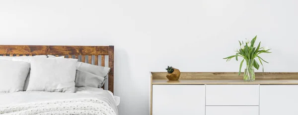 リネン 枕とベッドが備わり 明るい寝室のインテリアで白い壁にトップに立って上に花瓶の新鮮な切り花のサイド キャビネットの部分のクローズ アップ パノラマ 実際の写真 — ストック写真