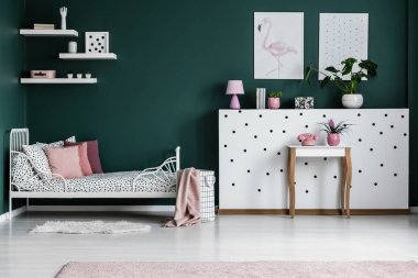Yeşil yatak odası iç desenli yatakta pembe yastık ile duvardaki posterler