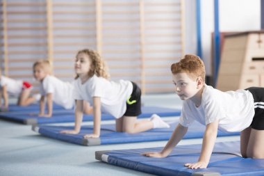 Genç çocuk ve bir spor salonu mat sınıf arkadaşları postural hataları önleme ile yardımcı olan kemerli geri inek yoga pozuyla öğrenme üzerinde duruldu