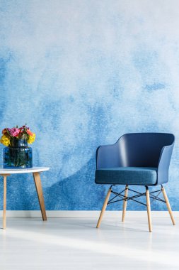 Lacivert koltukta en az oturma odası iç, yanındaki ahşap masa üzerinde renkli çiçekler