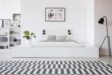 Siyah lamba ayakta beyaz bir platform bir yatak ve modern otel yatak odası iç üzerine bir monstera bitki yanında gerçek fotoğraf