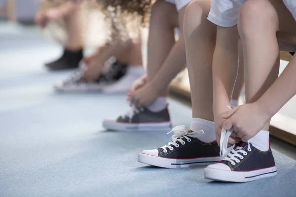 中にはベンチに座っているし 体育活動のためのスポーツの靴を結ぶことの学校の子供たちの足のクローズ アップ — ストック写真