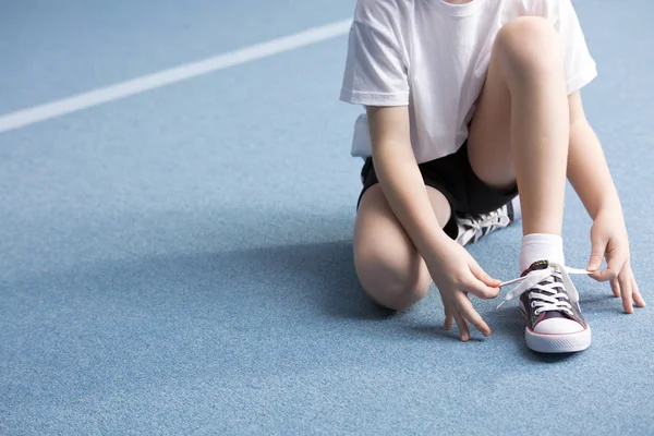 ジムで青い床に靴を結ぶ子供のクローズ アップ — ストック写真