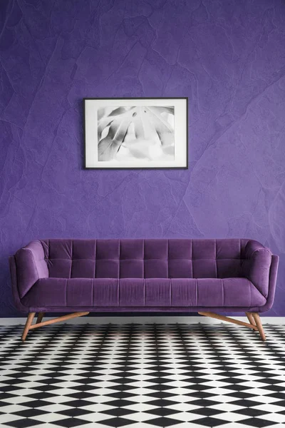 Poster on violet wall above suede sofa in living room interior with checkerboard floor