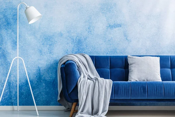 Navy blue sofa with blanket and pillow, lamp set on an ombre wall in a living room interior