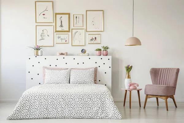 Dotted, double bed, paintings with gold frames and pink armchair set in a serene bedroom interior