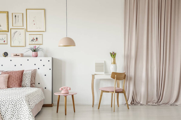 Wooden chair at dressing table in pastel pink bedroom interior with phone next to patterned bed