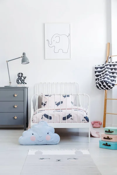 Blue cloud pillow in front of white bed next to grey cabinet in kid's bedroom interior. Real photo