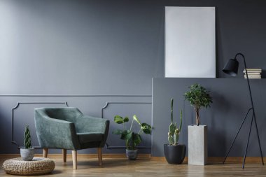 Kabarık yanındaki gri renkli düz poster mockup ile iç yeşil koltuk üzerinde bitki. Gerçek fotoğraf