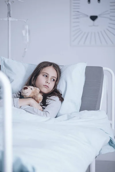 病院のベッドで寝ながらぬいぐるみを抱いて孤独な悲しい少女 — ストック写真