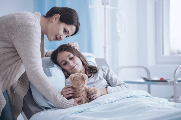 关心母亲给生病的女儿一个长毛绒玩具躺在病床上 — 图库照片