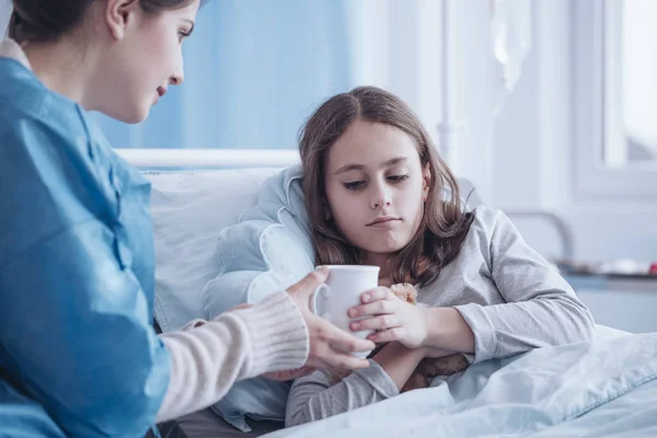 关爱母亲在门诊给生病的女儿送热茶 — 图库照片
