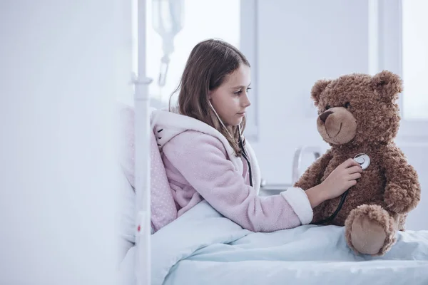 Gadis Sakit Dengan Stetoskop Memeriksa Boneka Beruang Tempat Tidur Rumah — Stok Foto