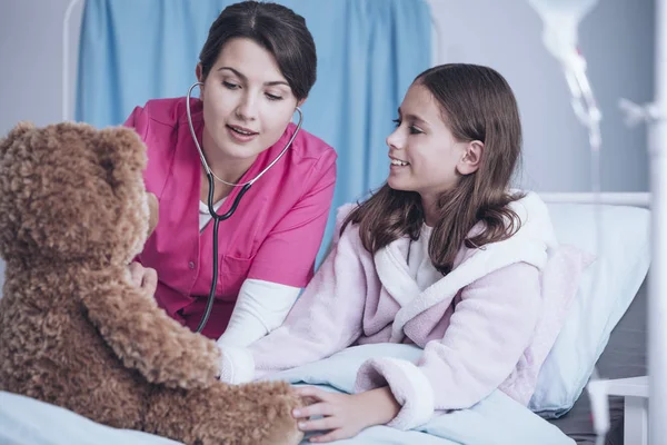 医生玩听诊器 检查一个长毛绒玩具和一个生病的女孩微笑 — 图库照片
