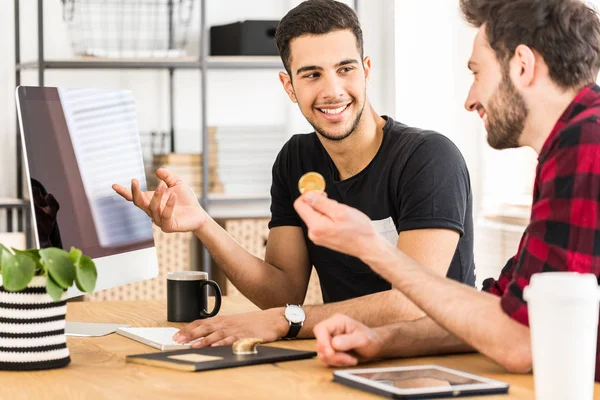 Friends sitting in an office at a desk while one is holding a bitcoin