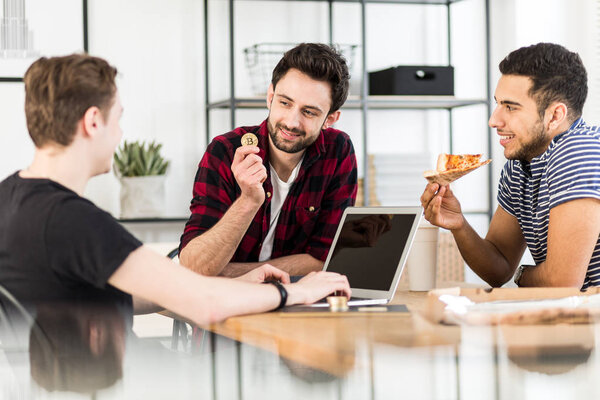 Man eating pizza and his friend holding a gold coin. Cryptocurrency concept
