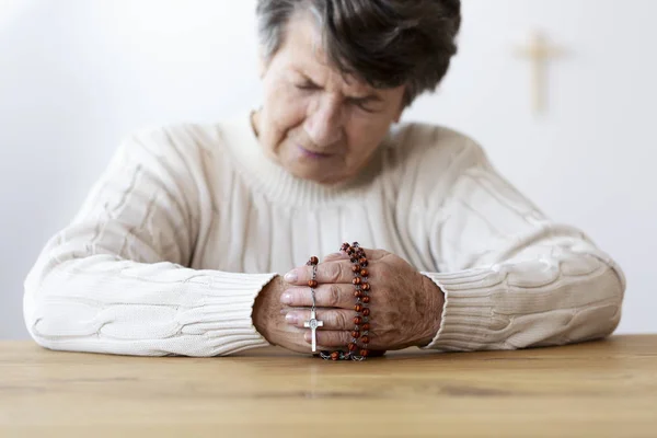 Religious senior woman praying with red rosary in the church. Focus on the hands
