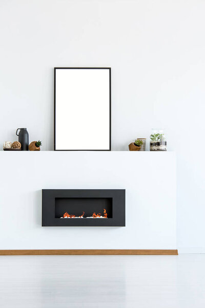 Mockup of empty poster above black fireplace in simple white living room interior. Real photo with a place for your graphic