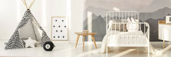 Patterned tent near white metal bed in kid's bedroom interior with mountain wallpaper