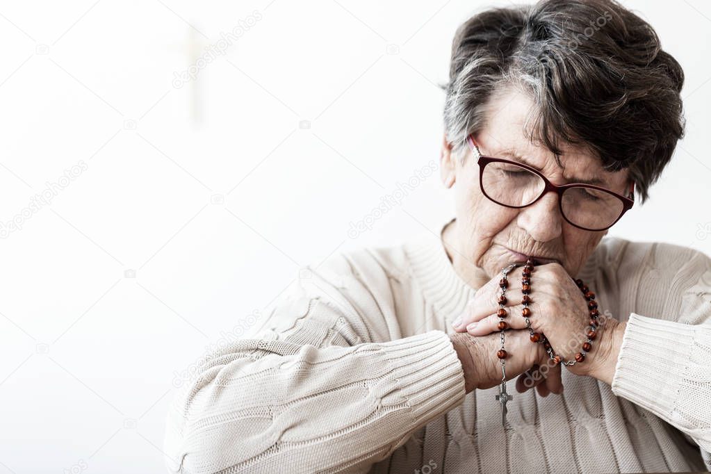 Catholic grandmother in melancholy praying to god with red rosary with cross