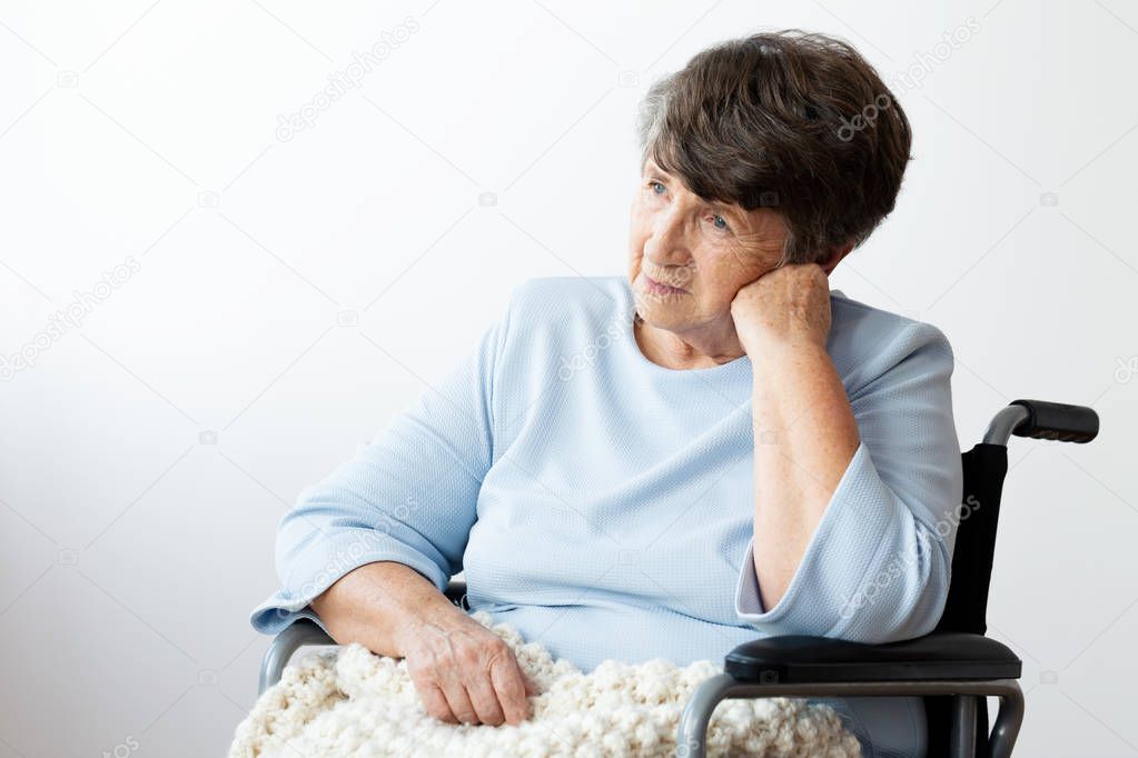 Sad disabled senior woman in a wheelchair against white background