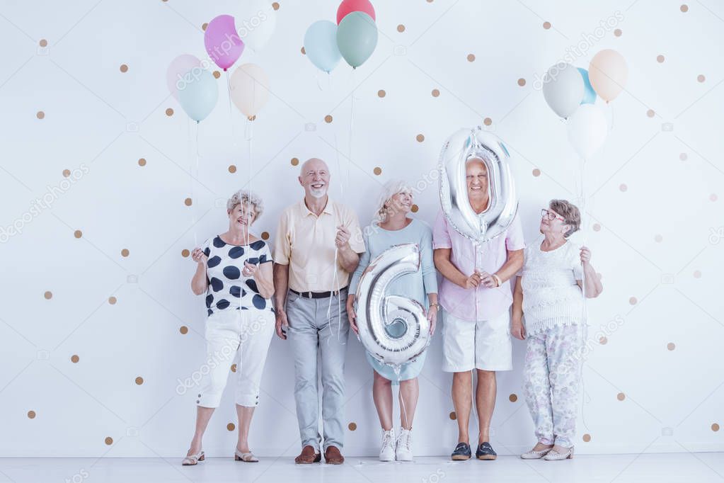 Enthusiastic elderly people with colorful balloons celebrating friend's birthday