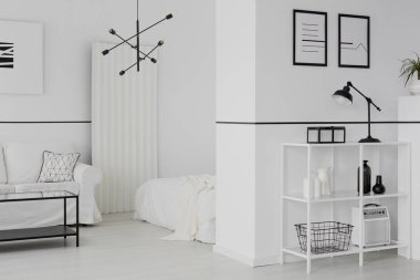 Bir raf duvara posterler beyaz açık alan iç kanepe ve yatak ile siyah lamba