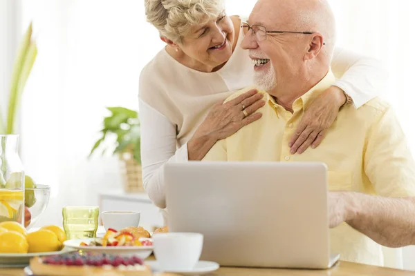 Happy elderly people using laptop while eating breakfast