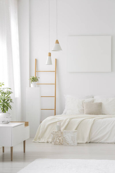 Copy space on empty poster above bed in white bedroom interior with lamps and wooden ladder