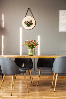 Ahşap masa gri yemek odası iç duvar ve cam vazo içinde sunulan taze çiçekler asılı lale poster yerleştirilen