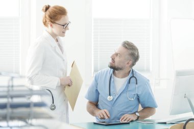 Ofiste çalışan ve onun yardımcısı söz ederken tablet kullanarak doktor