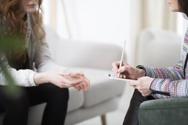 Cropped photo of a therapist writing down notes during therapy with her female patient