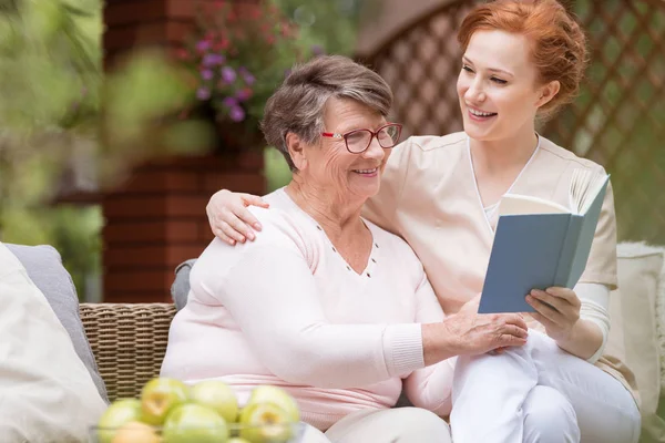 Cheerful Senior Woman Her Tender Caretaker Reading Book Together While — Stock Photo, Image