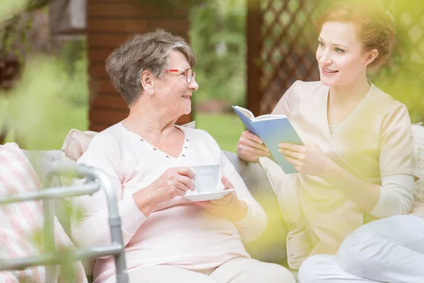 Friendly Caregiver Reading Book Senior Woman Drinking Tea Garden — Stock Photo, Image