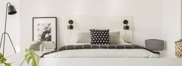 Black lamp standing by the platform with bed with pillows and white sheets, books, poster and small basket