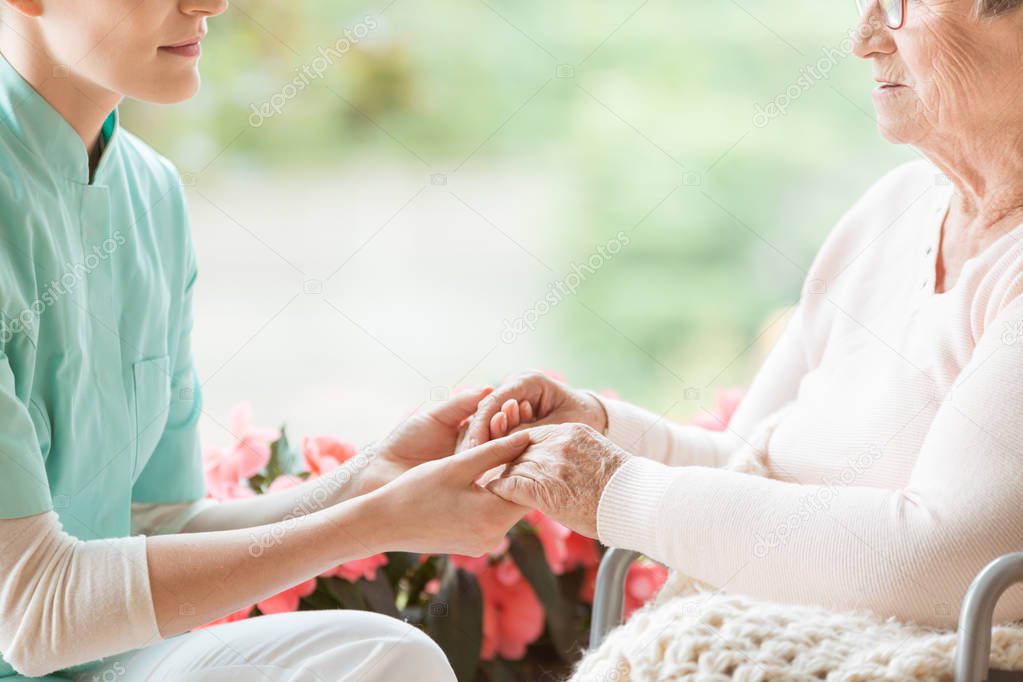 Nurse holding hands of disabled elderly woman in a wheelchair