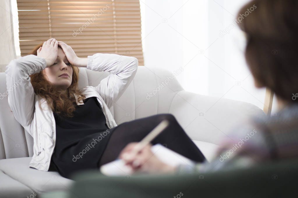 Depressed woman holding her head while sitting on a couch in a psychiatrist office