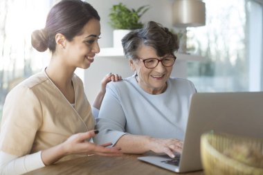 Bir dizüstü bilgisayarda Internet arama yaşlı bir kadın öğretim mutlu Yardımcısı