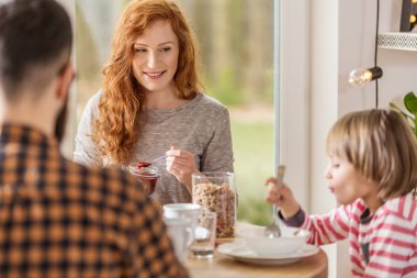 Genç aile büyük pencereli bir oturma odasında birlikte kahvaltı
