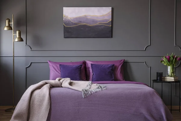 成形と灰色の壁に絵をエレガントな寝室のインテリアでバイオレット ベッドの上ピンクの毛布 — ストック写真