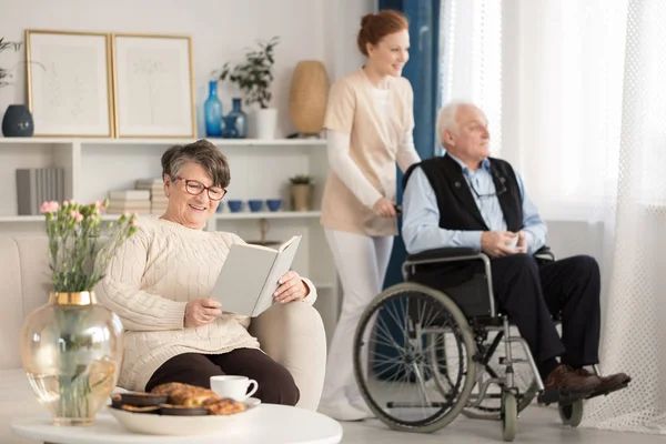 Gülümseyen kıdemli kadın bir bakım evinde onun kalmak sırasında bir kitap okuma