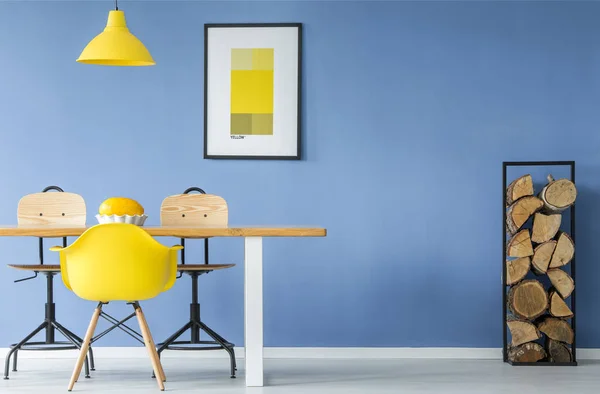 一张黄色的椅子和一盏悬挂在空地上的灯 最小的风格内部与一个瓜在桌子上 一堆木柴对蓝色墙上的一个样机海报 — 图库照片