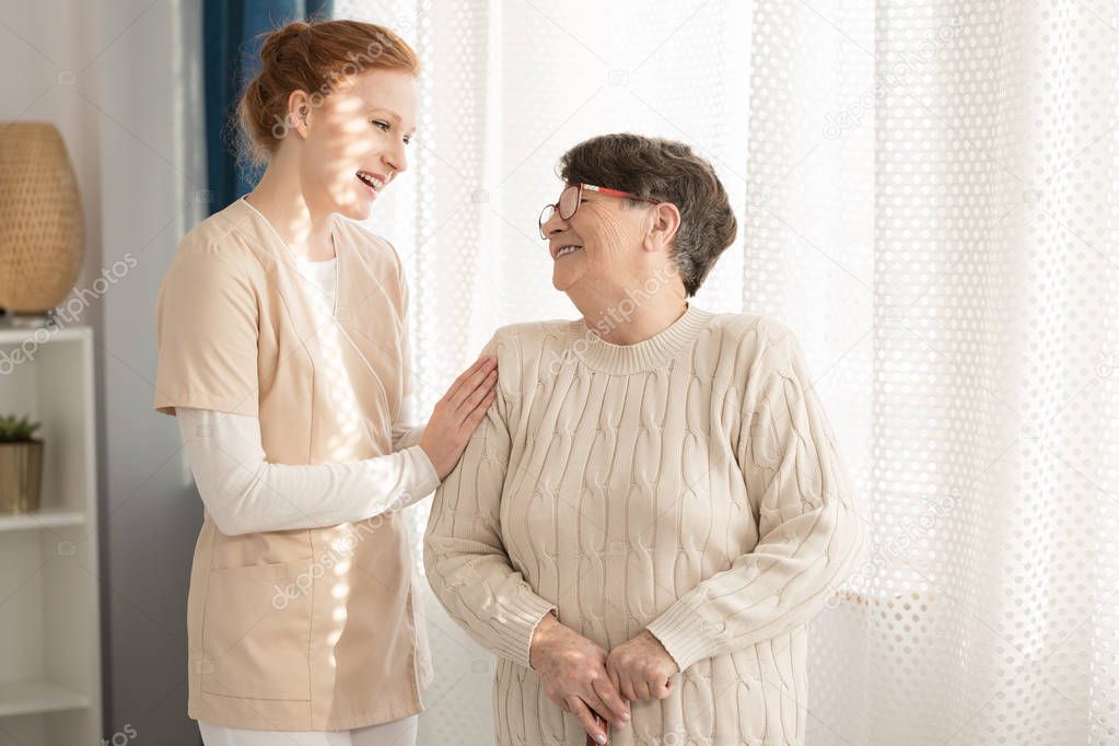 Smiling nurse taking care of a happy elderly woman in a nursing home