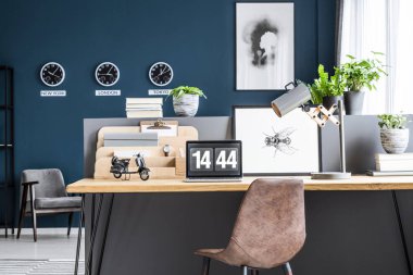 Kahverengi deri sandalye ayakta ahşap ev ofis masası lambası, poster ve koyu mavi salon iç içinde laptop ile tarafından