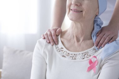 Meme kanseri şerit takan gülümseyen bir kadının omuzları ellerde close-up