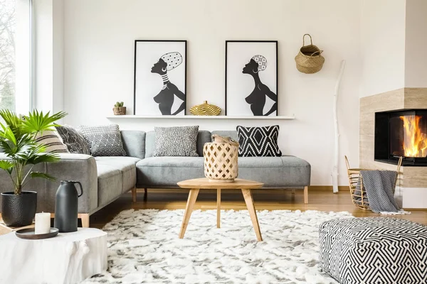 Patterned pouf next to wooden table in african living room interior with posters. Real photo