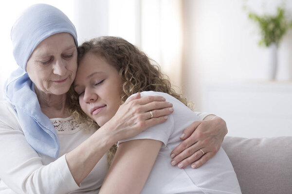 Daughter hugging sick elderly mother with cancer wearing a blue headscarf