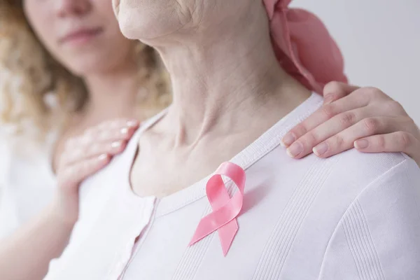 Woman with cancer wearing a pink ribbon, supported by her daughter